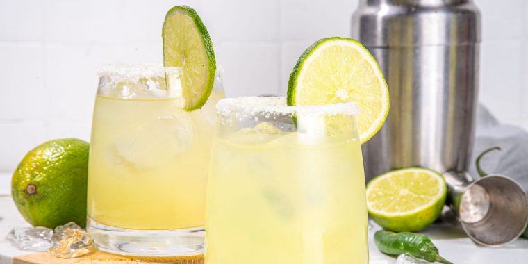 Alluring Mezcal Margarita garnished with lime and a salt rim featured against a white backdrop with a cocktail shaker and lime wedge