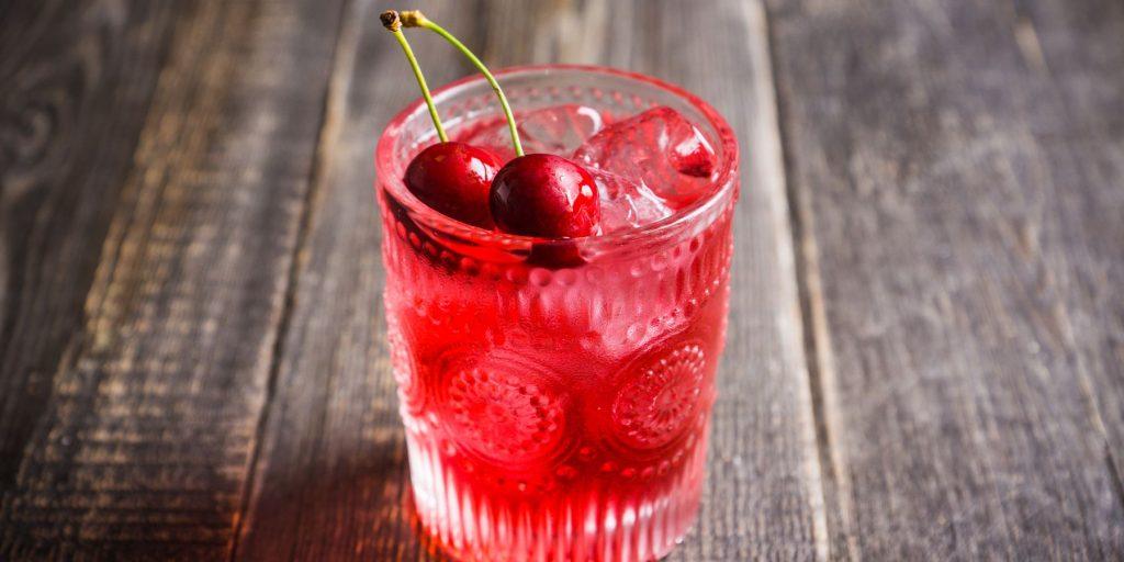 The beautiful Cherry Blossom cocktail in a rocks glass garnished with fresh cherries for an extra pop of color