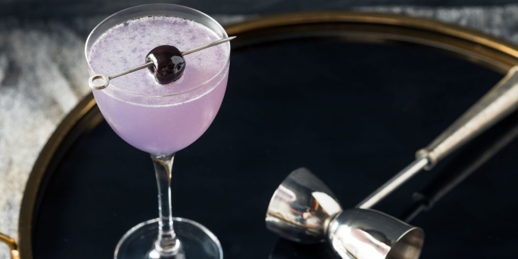 A top view of an Aviation Cocktail in a sleek cocktail glass, served on a serving platter with a silver cocktail jigger to the side