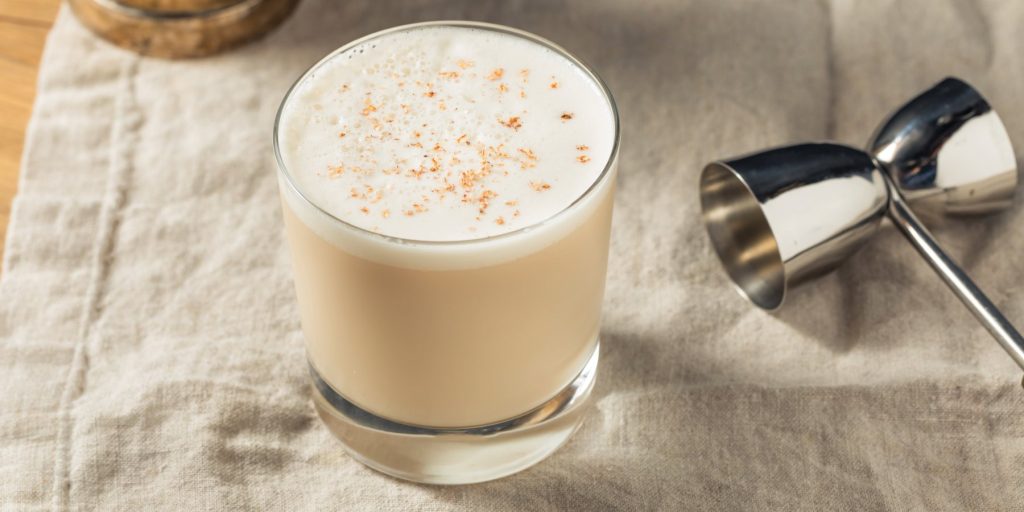 A Brandy Milk Punch cocktail in a rocks glass on a table with a cocktail jigger
