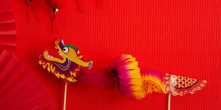 Red backdrop with a colorful paper dragon featured alongside an open fan and Chinese New Year trinkets