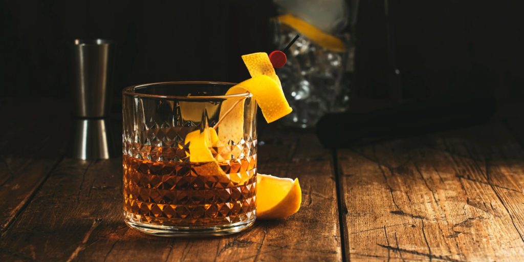 A Sazerac cocktail on a wooden table garnished with a lemon peel twist