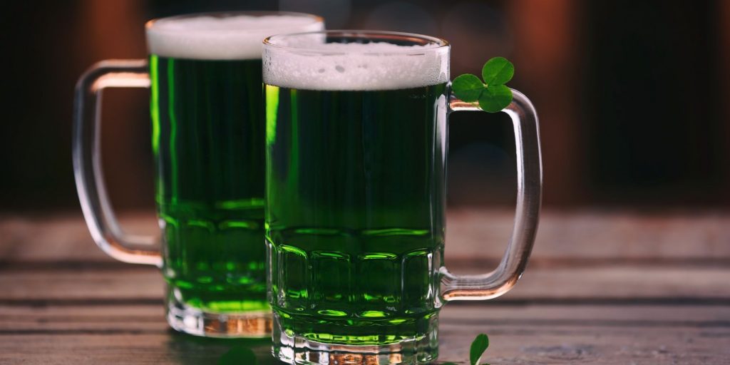 Two iconic green beers in tall pint glasses garnished with a shamrock, perfect for St Paddy's