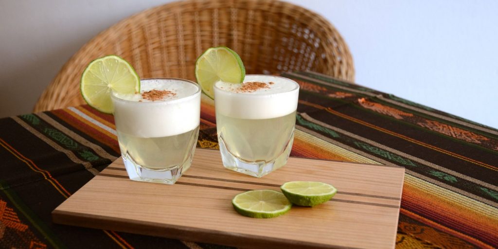 Two glasses of Mezcal Pineapple Sour cocktail on a wooden serving platter on a table with a wicker chair in the background