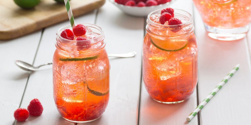 Two mason jars of Raspberry Lemon & Lime Ginger Beer Cocktail on a light wood surface