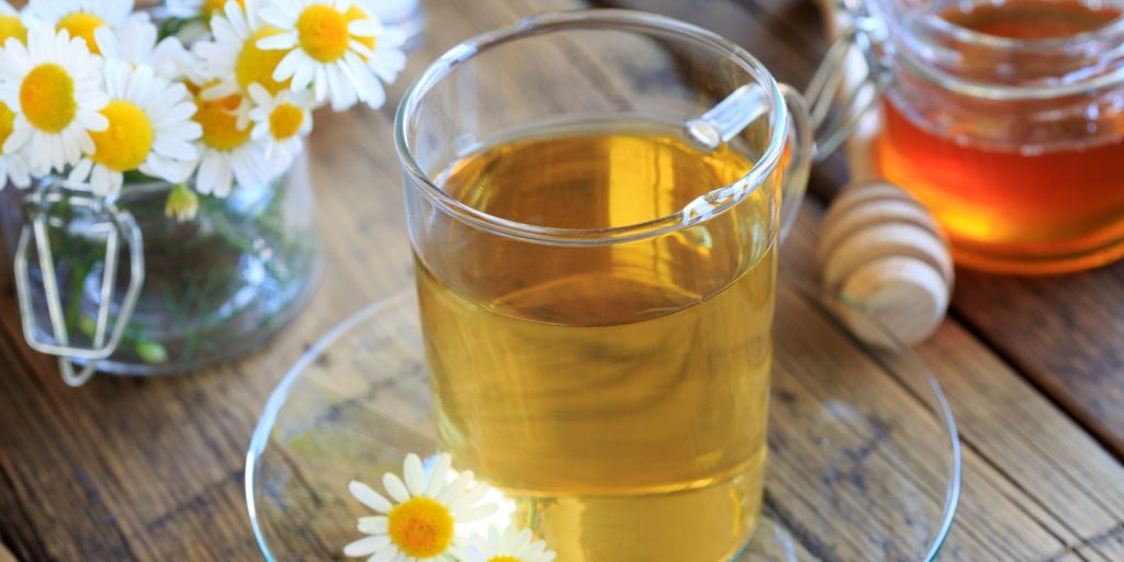 A cup fo Spring Buzz cocktail with a jar of honey and some camomile blooms to the side