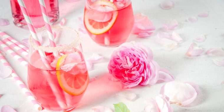 Three pretty pink Mother's Day cocktails arranged on a white backdrop with a pink rose and some petals scattered to add a little whimsy