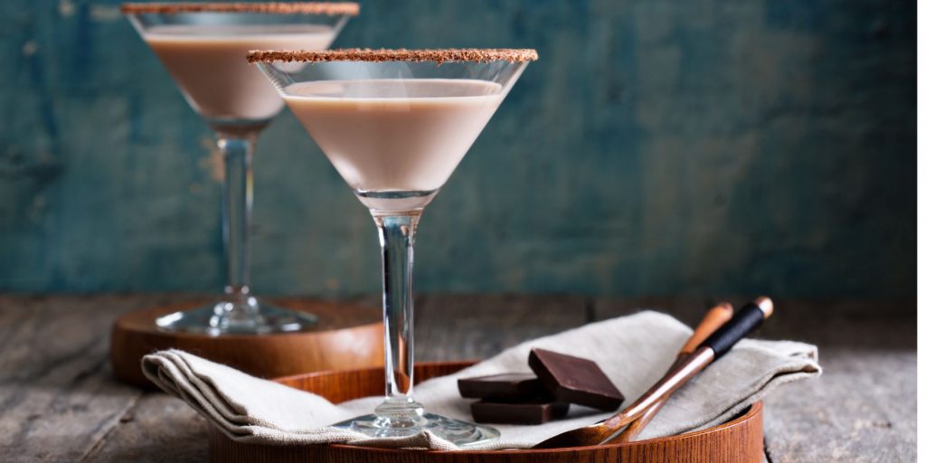 A front view of two Mini Egg Martinis on a wooden surface against a greenish blue backdrop