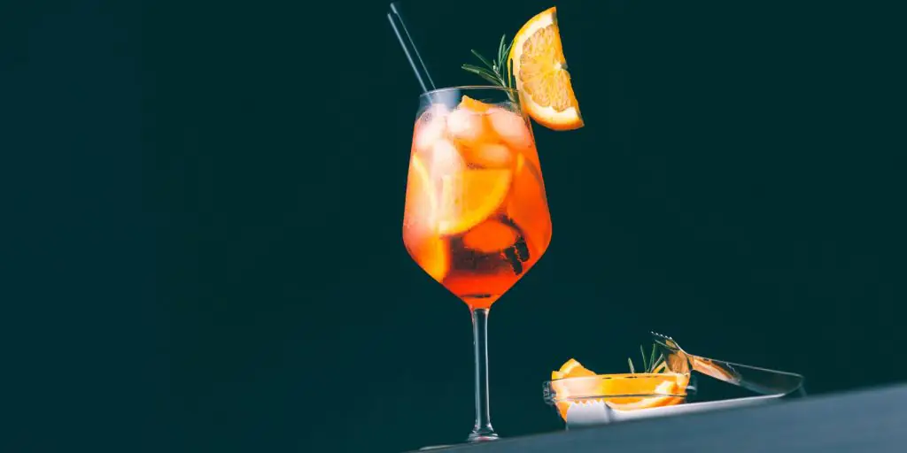 Tall refreshing orange colored cocktail garnished with a fresh slice of orange against a dark backdrop