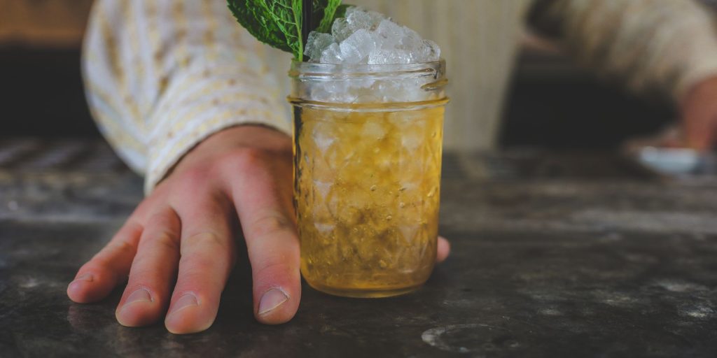Close-up of a man's hand holding a Honeysuckle Julep on a wooden surface
