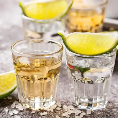 Close-up shot of two shot glasses of tequila garnished with lime wedges on a light grey surface