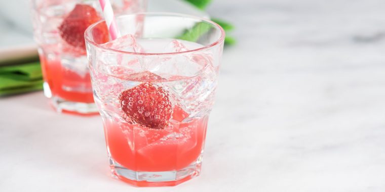 A pair of pretty pink-hued Shirley Temple cocktails garnished with cherries, standing on a white surface, one behind the other