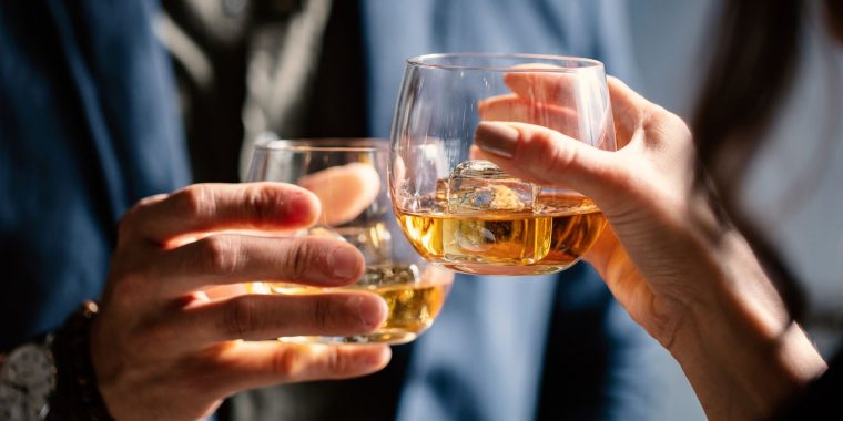 Close-up image of a couple clinking glasses of whiskey with clear ice