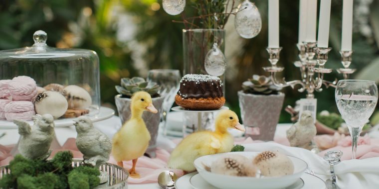 A beautiful Easter table set with crystal stemware and candles, and a few fluffy chicks having a whimsical moment in the midst of it all