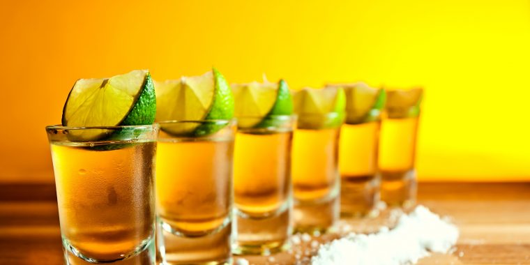 A row of tequila shots with lime wedges and salt