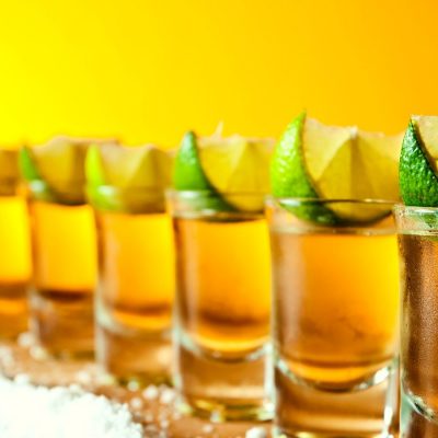 A row of tequila shots with lime wedges and salt