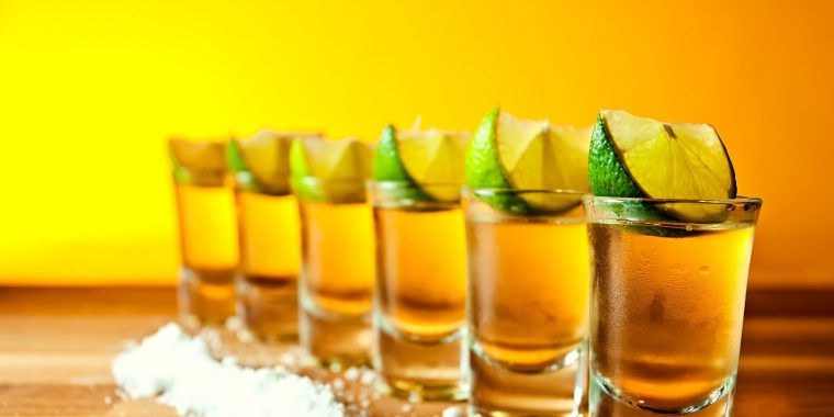 A row of tequila shots with lime wedges and salt