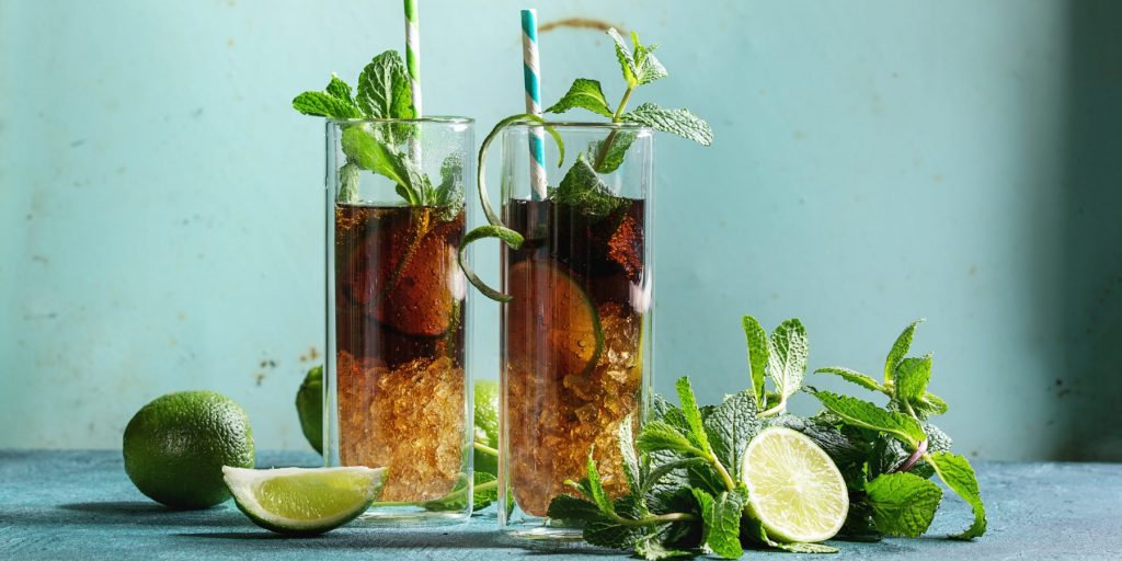 Two Cuba Libre cocktails served in a tall glasses with ice, lime and mint garnish