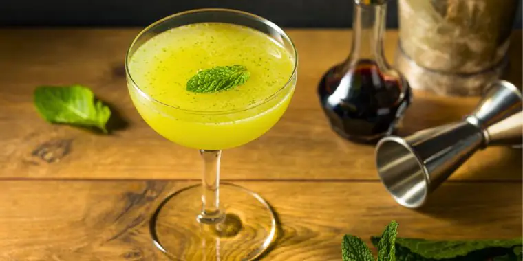 Top view of a Southside Cocktail speckled with green, and garnished with a fresh mint leave, presented on a rustic wooden surface served in a dainty coupe glass