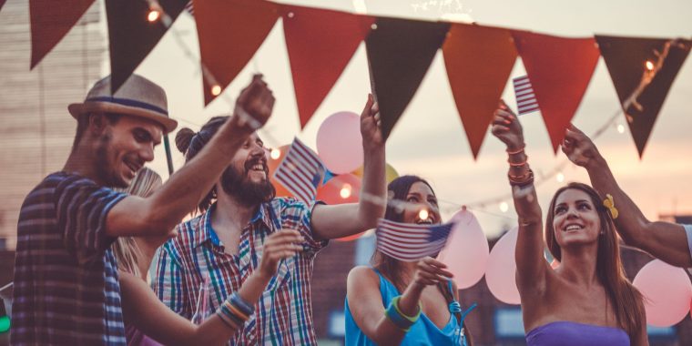 Close up of a group of friends waving small Americal flags and having a good time at dusk at a Memorial Day party