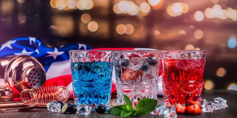A trio of red, white and blue Memorial Day cocktails on a counter with the American flag behind it