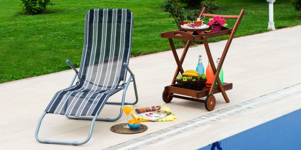 Outdoor bar cart on the edge of a pool next to a striped sun lounger