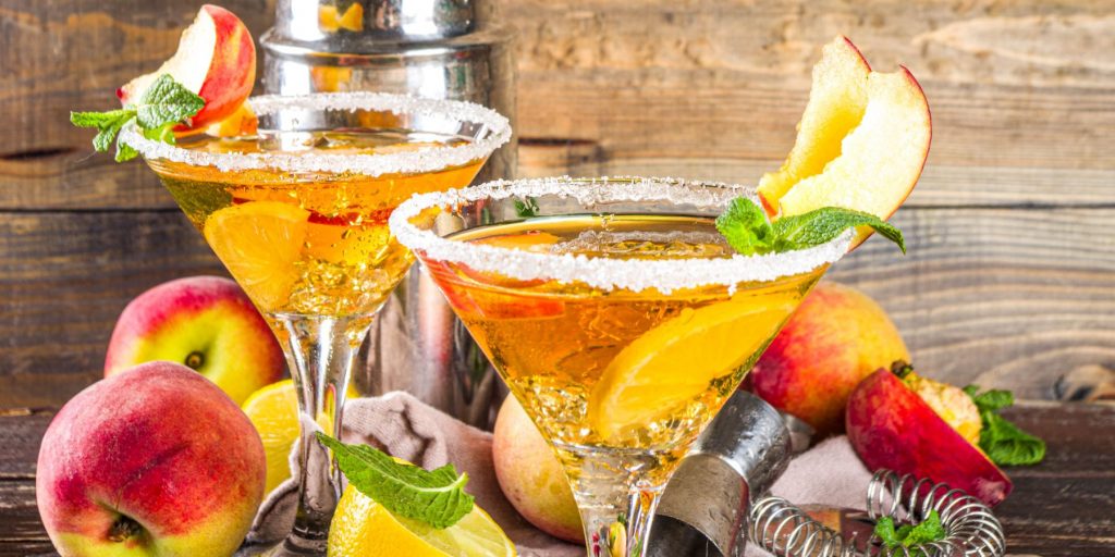 Close up of two sugar[-rimmed Peach Martinis against a rustic wooden backdrop