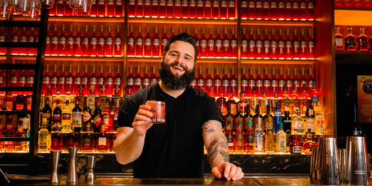 A mixologist holding a cocktail while standing behind the bar