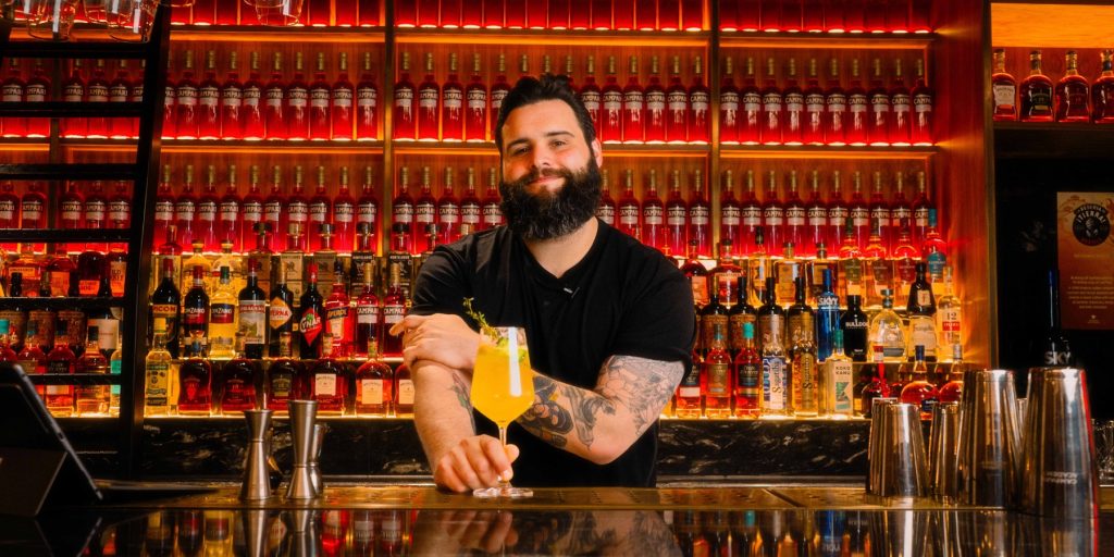 Mixologist holding an Energetic Gardener cocktail behind the bar