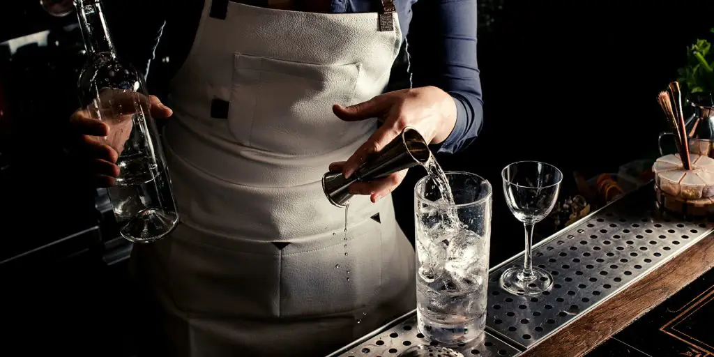 Woman pouring London dry gin into a glass with ice