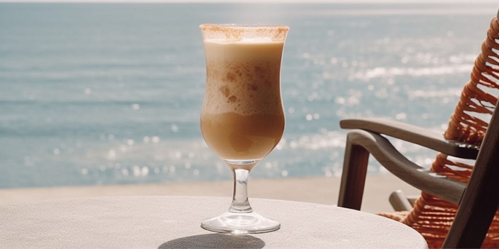 A creamy Bushwacker cocktail on a table next to a deckchar at the oceanside overlooking the sea on a sunny day