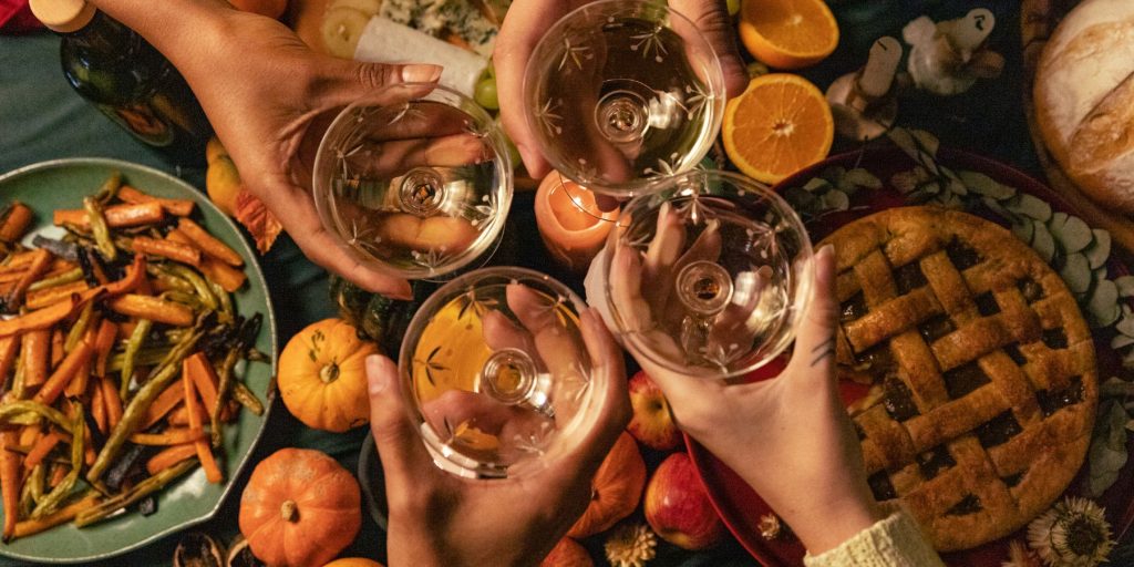Top view of a group of friends clinking coupe glasses of bubbly together over a Friendsgiving table dressed in fall colours