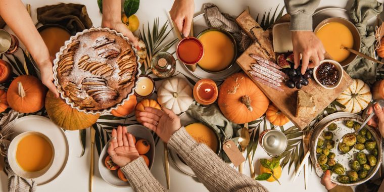 Top view of a very festiive Friendsgiving table dressed in wonderful fall colours with friends sharing food and passing bowls to one another