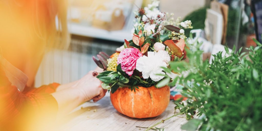 Side view of a woman creating Friendsgiving decor by adding fresh flowers to a hollowed out pumpkin
