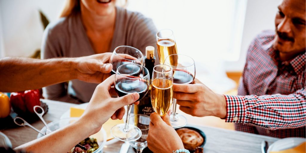 Group of friends clinking their glasses together over a Friendsgiving table in a light bright home lounge