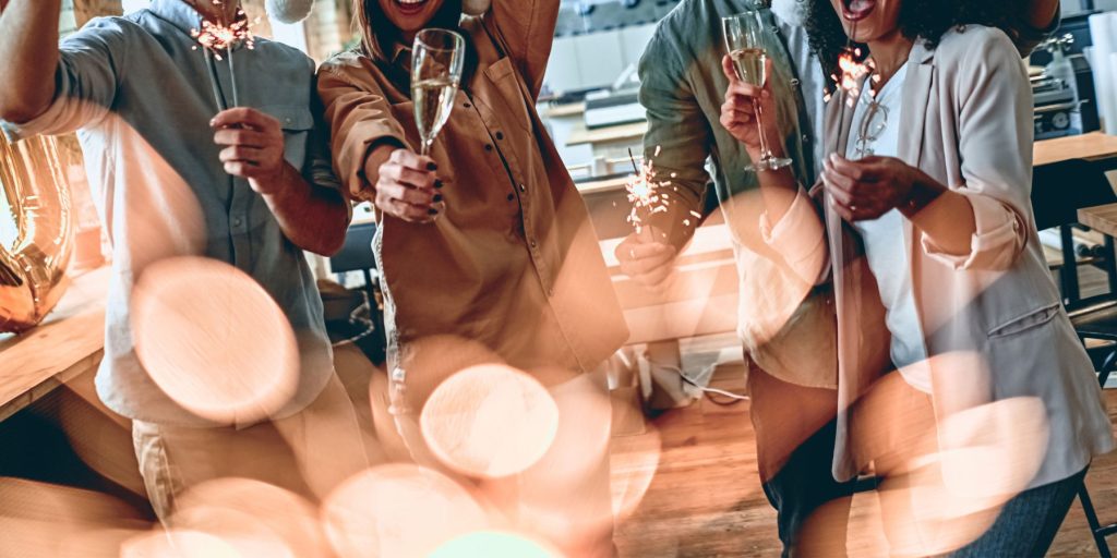 Close up image of co-workers clinking together festive cocktails in a bright modern office space