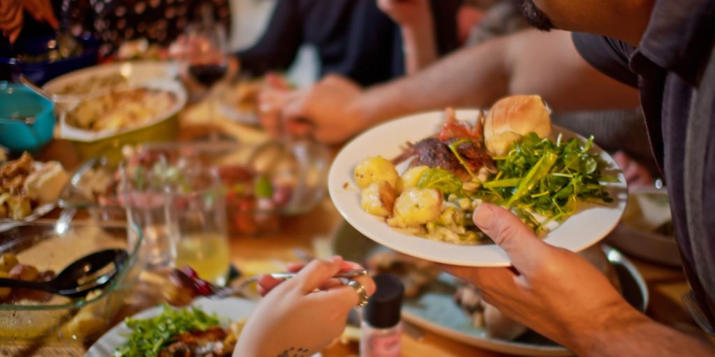 Close up of a group of co-workers dishing up some holiday food around a potluck table