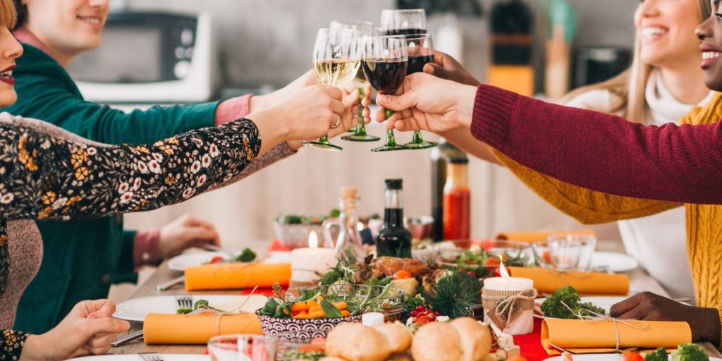 Close up of friends clinking together glasses over a festive table filled with all sorts of holiday foods 