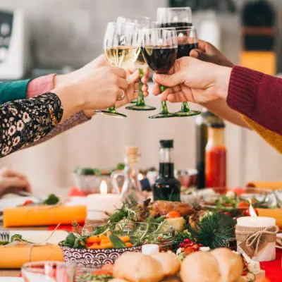 Close up of friends clinking together glasses over a festive table filled with all sorts of holiday foods