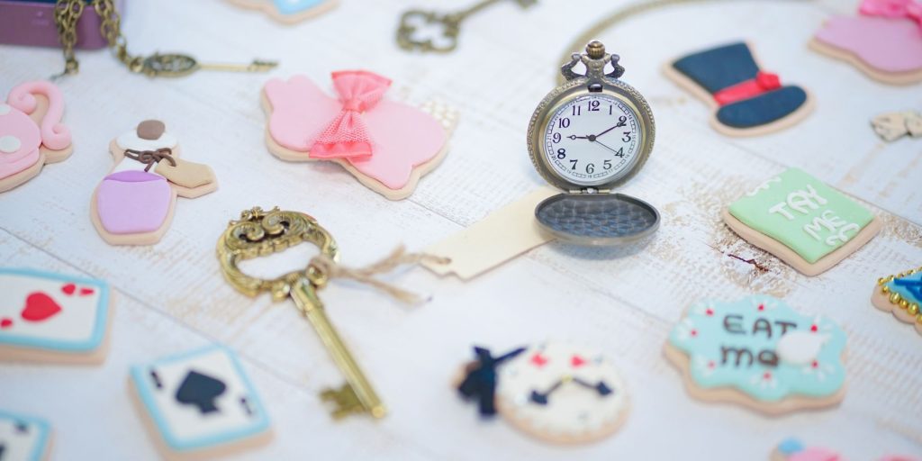 A variety of Mad Hatter Tea Party accessories laid out on a white surface, including keys and pocket watches
