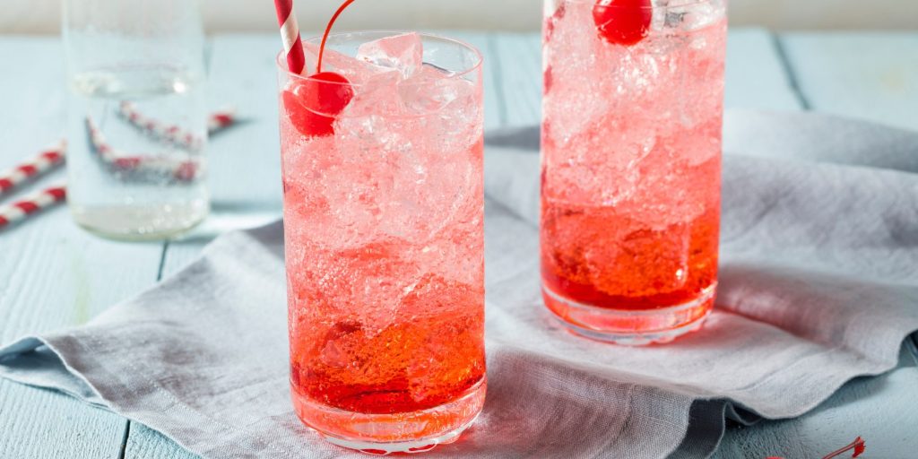 Close up of two pink Irish Rose cocktails in tall glasses, garnished with red cherries