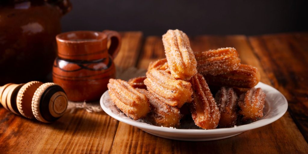 Front view of a batch of fresh churros presented on a white plate on a wooden surface