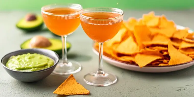 Two Naked and Famous Cinco de Mayo cocktails served with nachos and guacamole