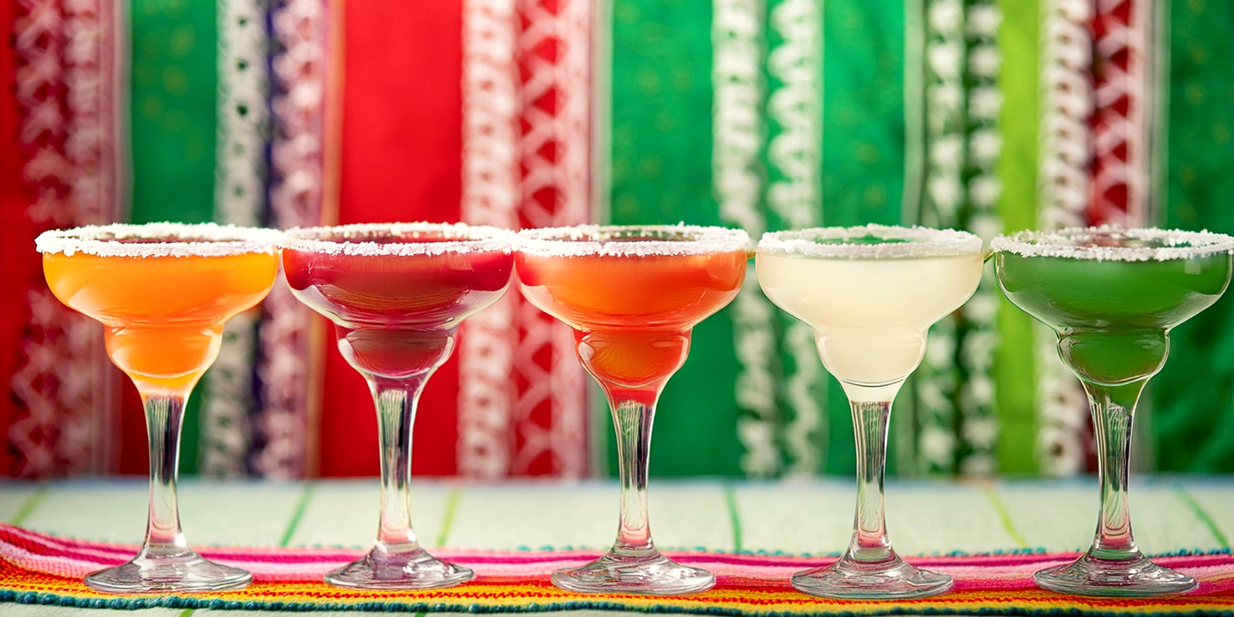 Colorful Margarita cocktails in a row with a Cinco de Mayo themed wallpaper in the background
