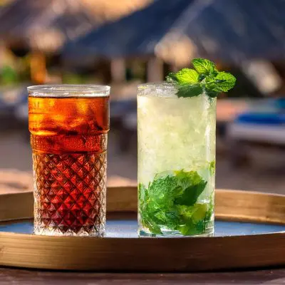 A Cuba Libre and a Mojito on a tray in a beach setting