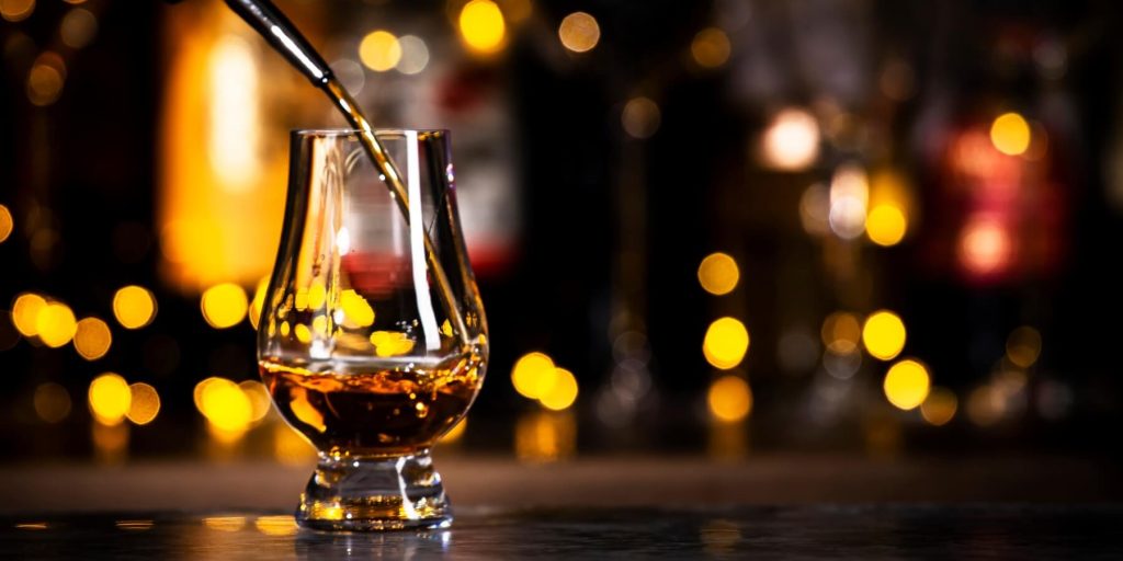 Amber-hued brandy de Jerez being poured into a tulip-shaped tasting glass, set against a festive background of blurred golden lights, photo by 5ph/Adobe Stock