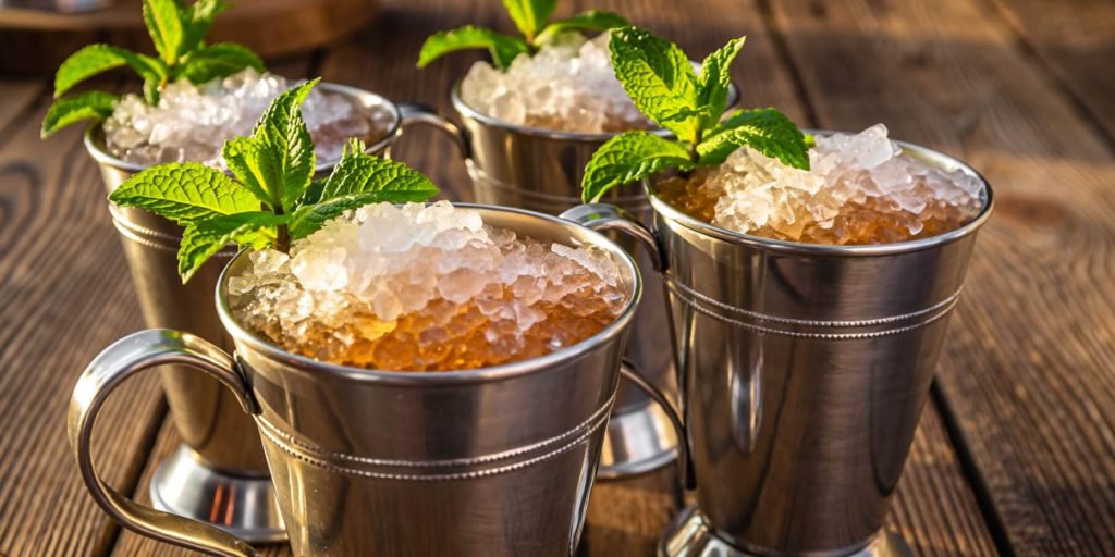 Three stainless steel tumblers of Mint Juleps with crushed ice and mint sprigs