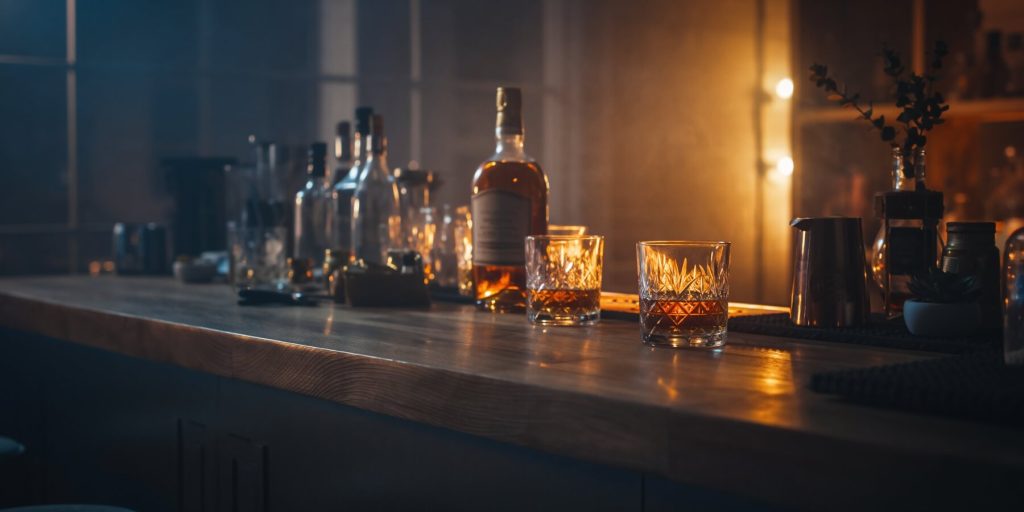 A cozy bar set up at home with moody lighting two glasses of whiskey with bottles in the background