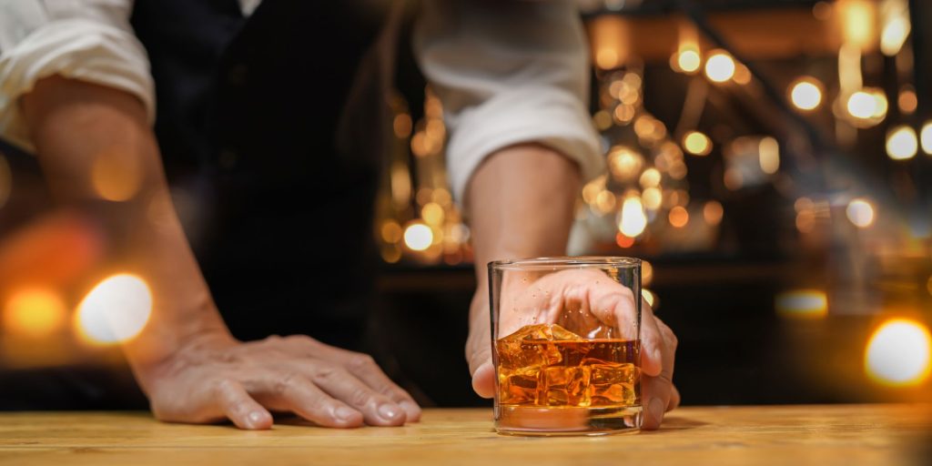 A close up shot of a bartender serving a bourbon on the rocks
