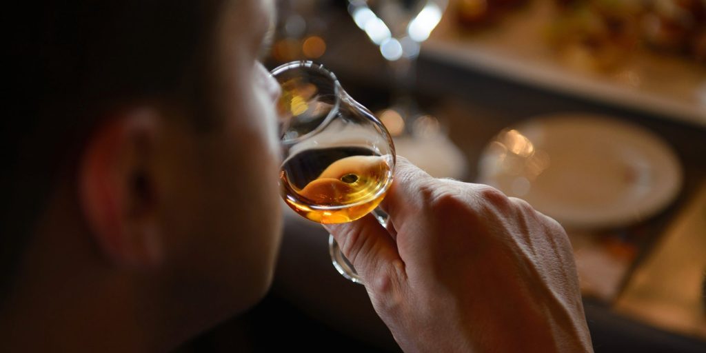A over the shoulder shot of a man nosing a glass of whiskey